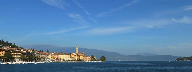 Trip Restplatzbörse beliebte Urlaubsziele am Gardasee -  Mit einer Fläche von 370 km² ist der Gardasee der größte See Italiens. Es liegt am Fuße der Alpen und erstreckt sich über drei Staaten: Lombardei, Venetien und Trentino. Die maximale Tiefe des Sees beträgt 346 m, er hat eine längliche Form und sein nördliches Ende ist sehr schmal. Dort ist der See von den Bergen der Gruppo di Baldo umgeben. Du trittst aus deinem gemütlichen Hotelzimmer und es begrüßt dich die warme italienische Sonne. Du blickst auf den atemberaubenden Gardasee, der in zahlreichen Blautönen schimmert - von tiefem Dunkelblau bis zu funkelndem Türkis. Majestätische Berge umgeben dich, während die Brise sanft deine Haut streichelt und der Duft von blühenden Zitronenbäumen deine Nase kitzelt. Du schlenderst die malerischen, engen Gassen entlang, vorbei an farbenfrohen, blumengeschmückten Häusern. Vereinzelt unterbricht das fröhliche Lachen der Einheimischen die friedvolle Stille. Du fühlst dich wie in einem Traum, der nicht enden will. Jeder Schritt führt dich zu neuen Entdeckungen und Abenteuern. Du probierst die köstliche italienische Küche mit ihren frischen Zutaten und verführerischen Aromen. Die Sonne geht langsam unter und taucht den Himmel in ein leuchtendes Orange-rot - ein spektakulärer Anblick.